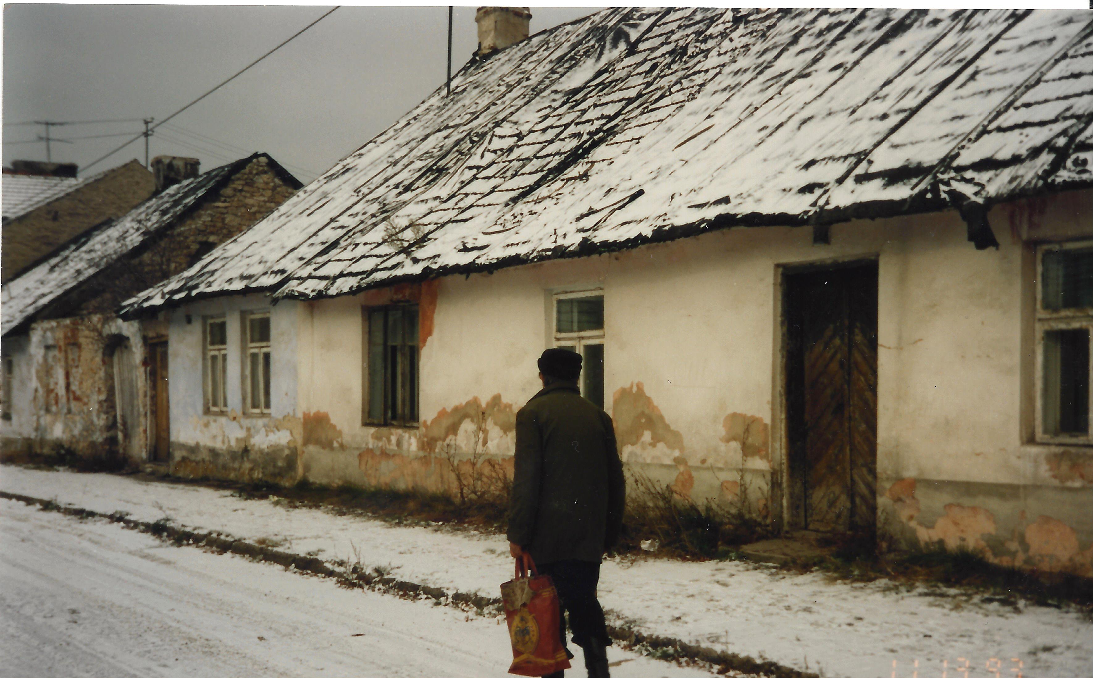 A person walking down the street in front of an old house.