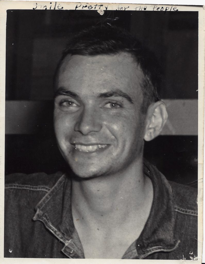 Smiling man in denim jacket, black-and-white photo.